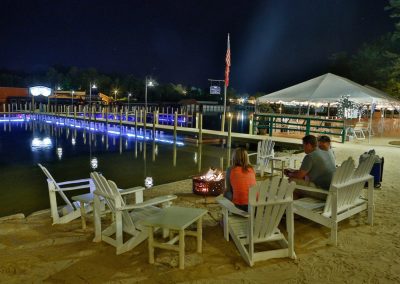 Guests in Adirondack chairs around a beach firepit