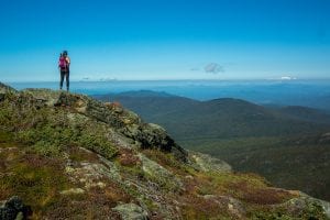A stunning view of a hiker near the top of a rugged foothill at the White Mountains National Forest.